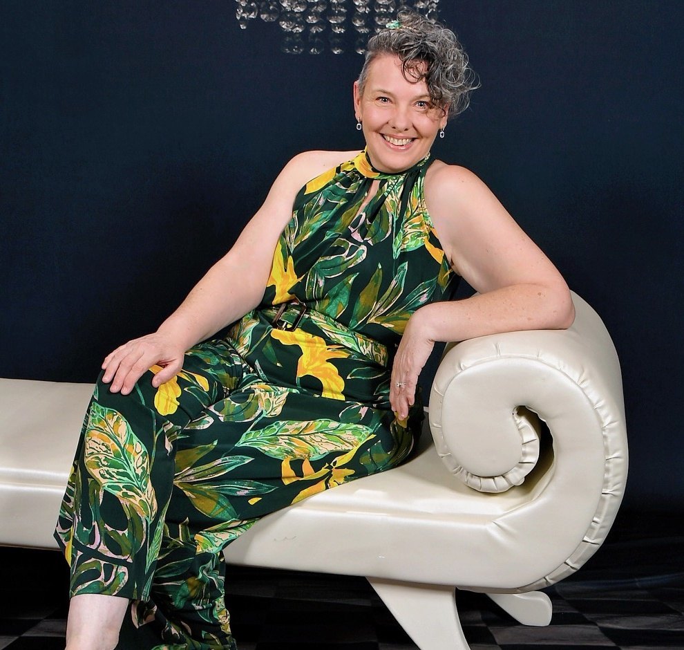 Stacey Pettitt, founder of Organised Apps Lab, seated in a green print jumpsuit against a navy wall